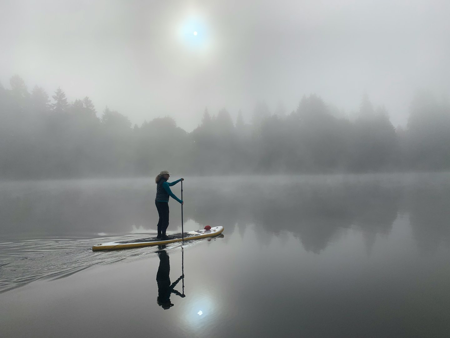 Person paddling a paddleboard on a foggy lake.